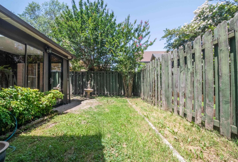 Manicured lawn area featuring a tall privacy fence, established shrubbery, and mature trees