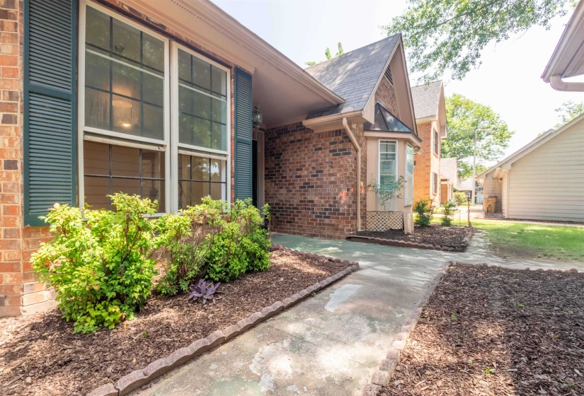 Brick exterior with dark green louvered shutters and a concrete walkway