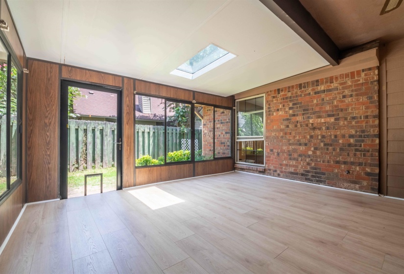 Bright sunroom featuring light wood-finish flooring, a skylight, and extensive window panels