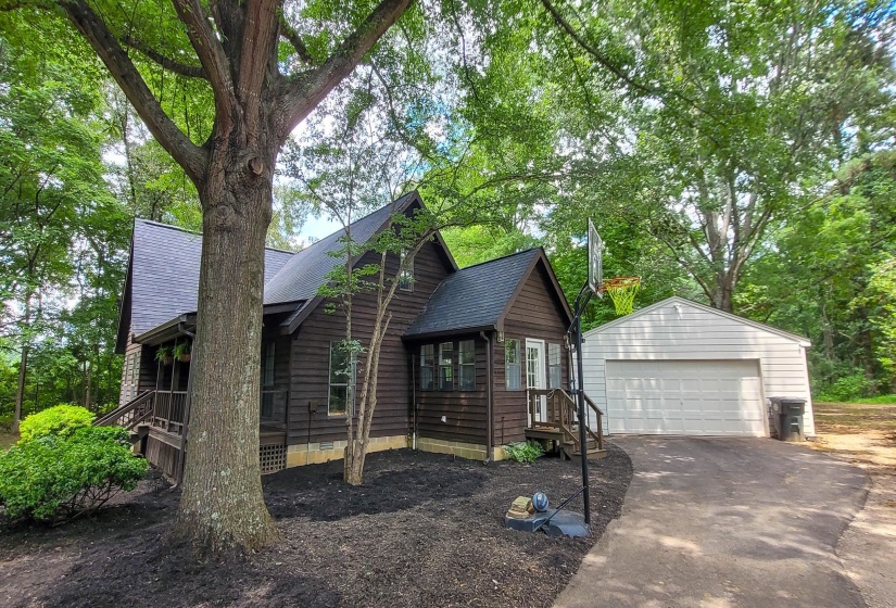 Wood-sided residence featuring a covered porch, detached two-car garage with white overhead door, and mature trees on the property