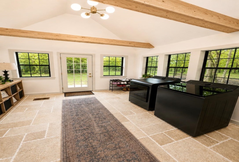 Spacious utility room featuring a vaulted ceiling with exposed wood beams, a contemporary chandelier, and large-pane windows