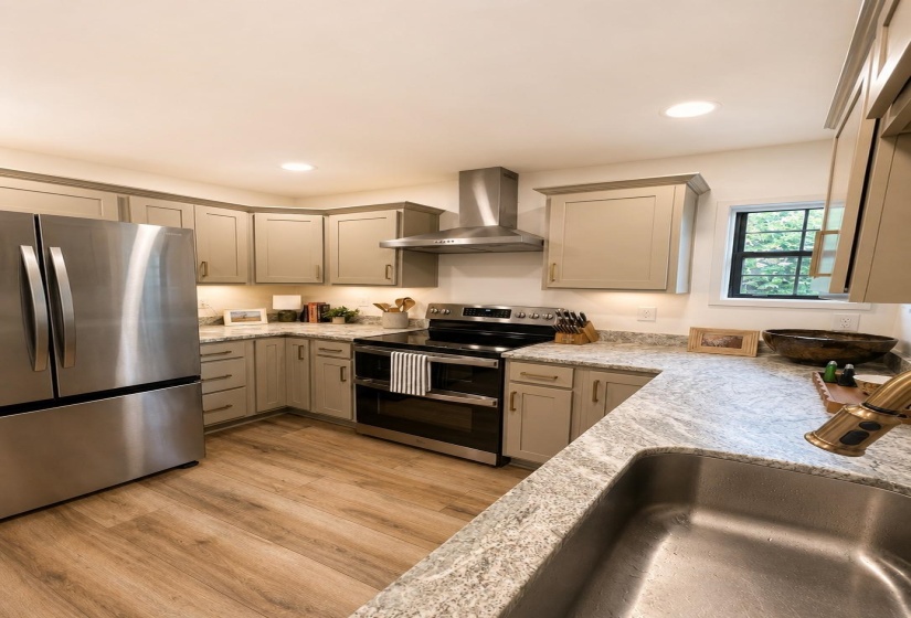 Contemporary kitchen featuring wood-finish flooring, light-toned cabinetry with crown molding, stainless steel appliances, and mottled countertops
