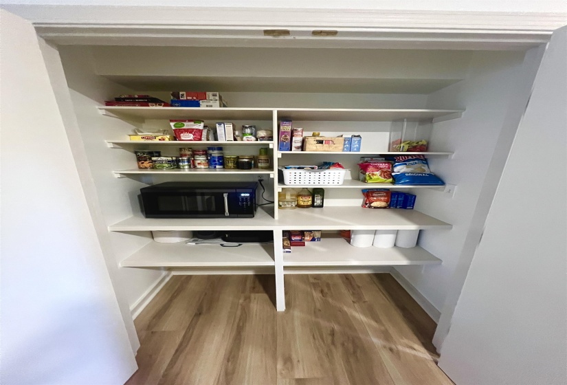Built-in pantry featuring white shelving, wood-finish flooring, and ample storage space