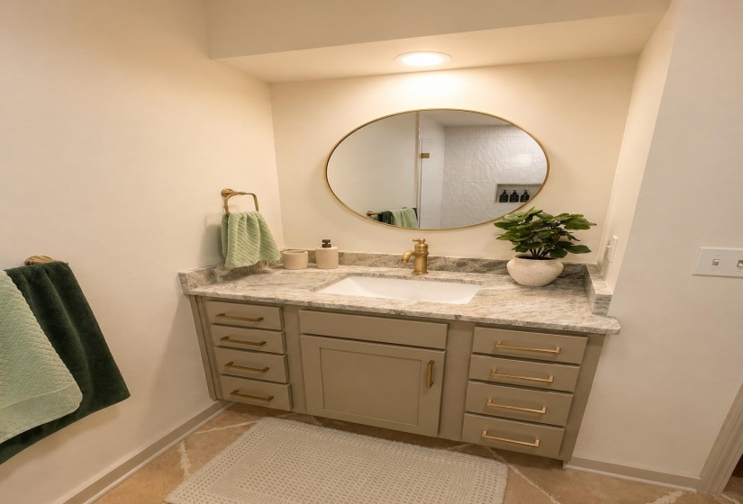 Vanity with undermount sink set in a light-toned countertop, complemented by a large circular mirror and brass-finish fixtures