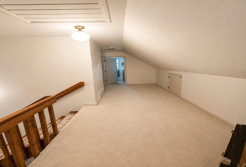 Attic hallway featuring plush neutral carpeting, a wooden banister, and a sloped ceiling