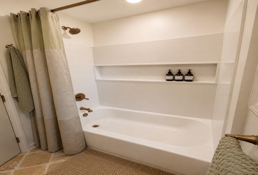 Bathtub with subway tile surround, integrated shower niche, and bronze fixtures