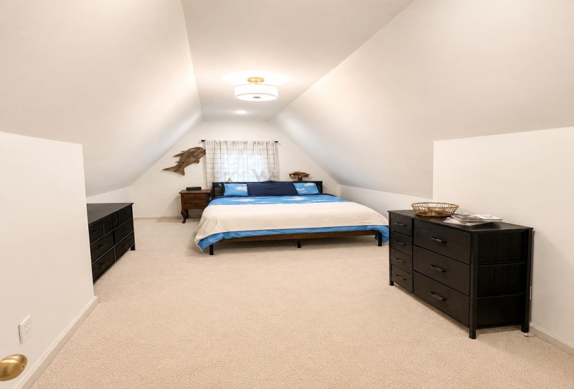 Attic room featuring a vaulted ceiling with a central flush-mount light fixture and light-toned carpeting