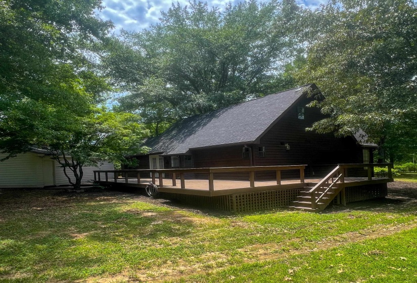 Expansive exterior deck featuring wood railing and steps, lattice skirting, and a dark brown wood-sided house with a black shingle roof