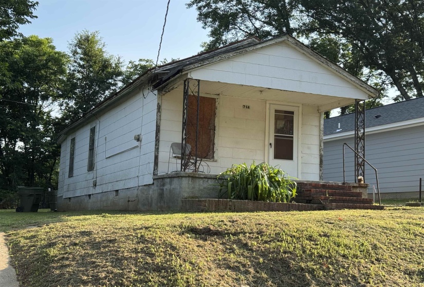 Single-story residence featuring white siding, a covered front porch with decorative metal columns, and brick stairs