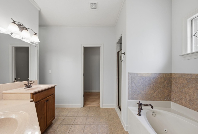 Bathroom featuring a dual vanity with integrated sinks and a light-colored countertop, a jetted tub with decorative tile surround, a separate glass-enclosed shower, and tile flooring