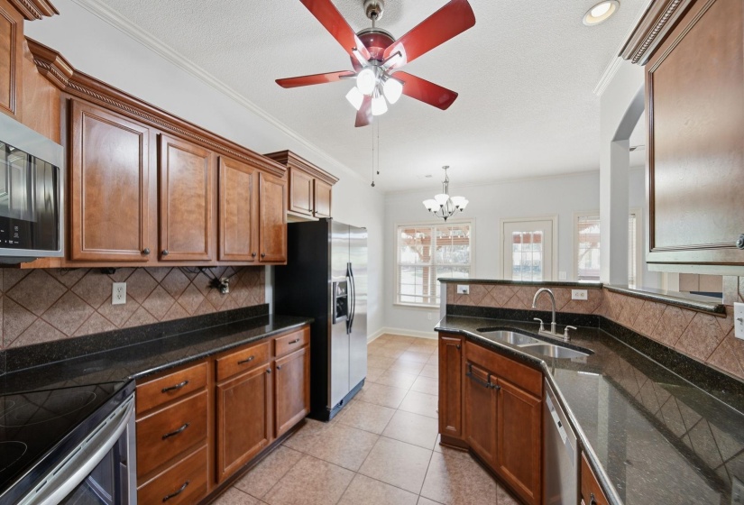 Kitchen featuring wood cabinetry, dark granite countertops, stainless steel appliances, and a diagonal tile backsplash