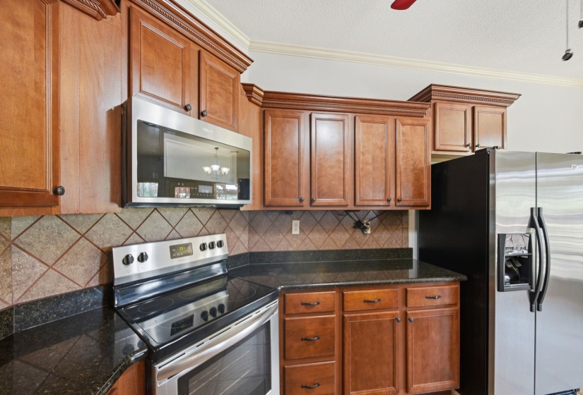 Kitchen featuring wood cabinetry, stainless steel appliances, dark granite countertops, and a tiled backsplash
