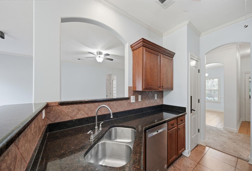 Kitchen featuring a double basin stainless steel sink, dark granite countertops, and coordinating backsplash