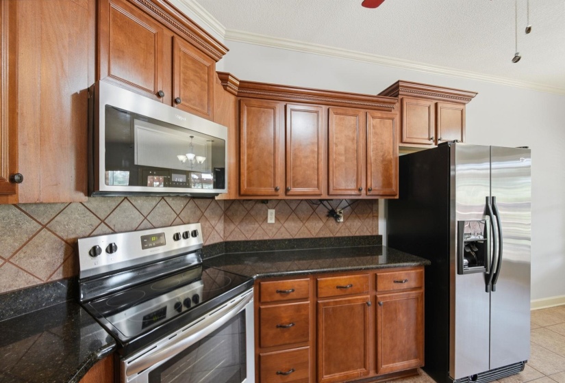 Kitchen featuring rich wood cabinetry, dark stone countertops, stainless steel appliances, and a tiled backsplash