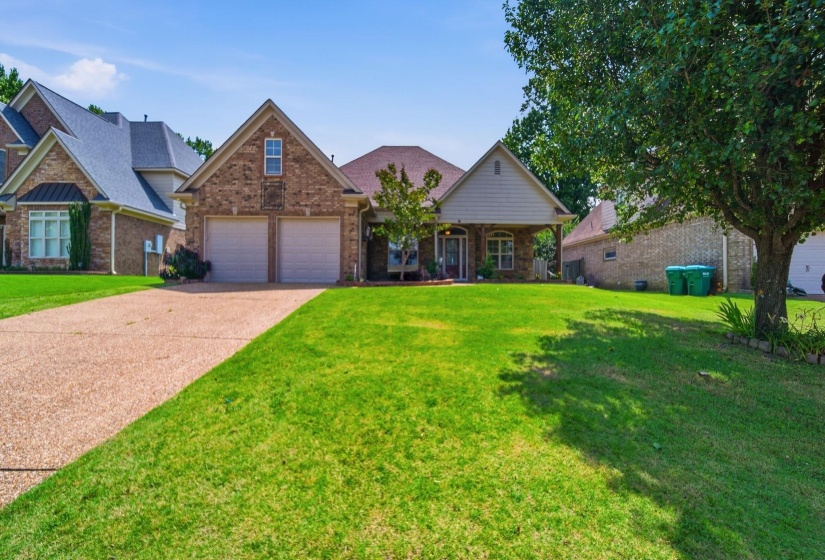 Brick exterior with a gabled roofline, featuring a two-car garage with individual doors, a covered porch entry, and a expansive front lawn