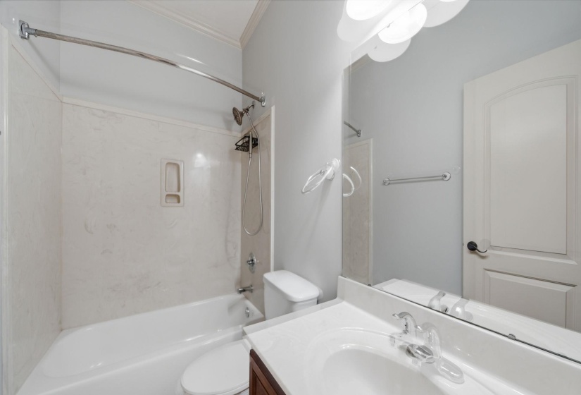 Bathroom featuring a white tub/shower combination with a curved shower rod, a dark wood-finish vanity with a white countertop and integrated sink, a large wall-mounted mirror, and a white interior door with a paneled design