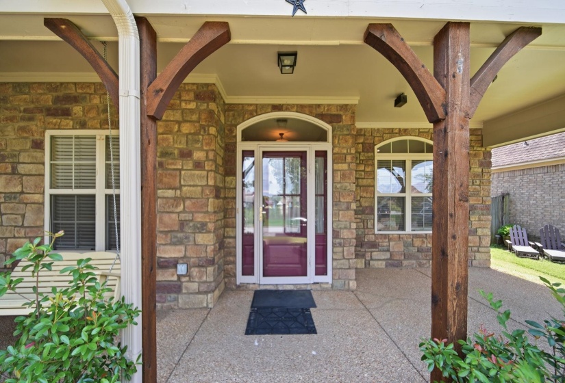 Stone facade home featuring a covered front porch with exposed wood beams, an arch-top entry door with glass panels, an arched window, and a concrete aggregate porch