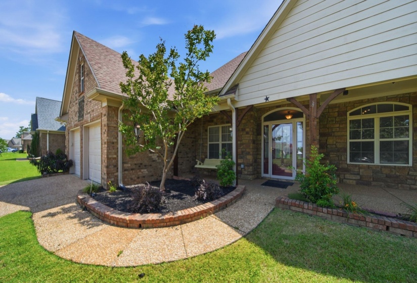 Brick and stone exterior featuring a covered front porch with timber posts, an arched entry door with sidelights, and a two-car garage with light doors