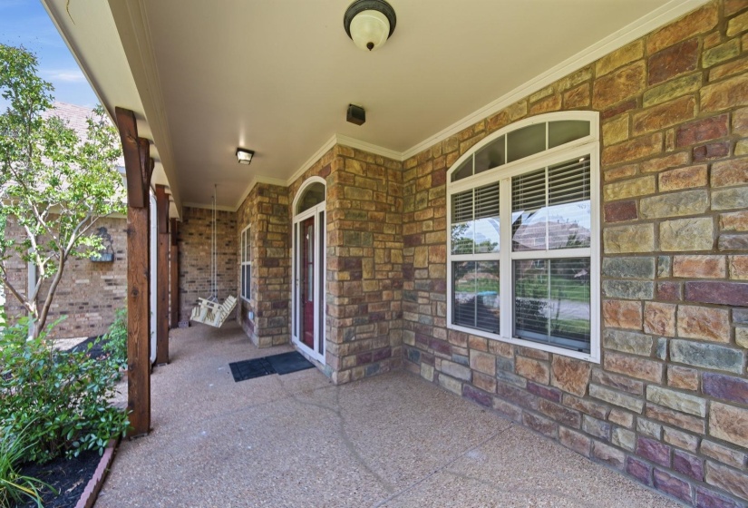 Stone facade with an arched entry door and a covered front porch featuring exposed wood beams, overhead lighting, and an arched picture window