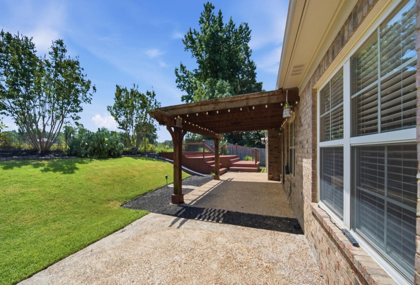 Expansive backyard featuring a concrete patio, wood pergola with string lights, and a raised wooden deck