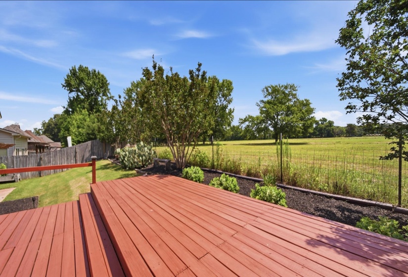 Multi-level red-stained wood deck featuring built-in railing and views of a verdant field