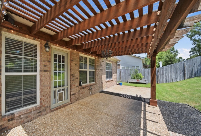 Covered patio featuring a wood pergola with integrated string lights, exposed aggregate concrete flooring, and a brick exterior