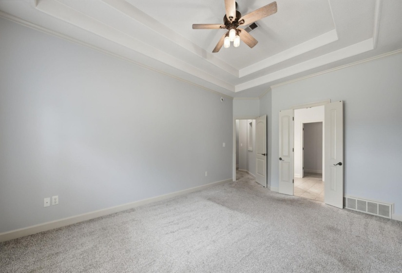 Spacious room featuring a tray ceiling with crown molding, a ceiling fan with light fixture, light gray carpeting, and double French doors with dark hardware