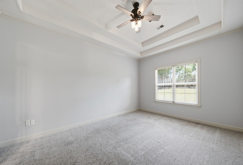 Primary Bedroom featuring tray ceilings, neutral wall paint, and light-colored carpeting