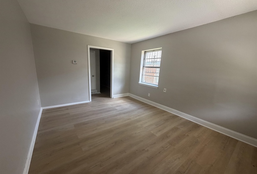 Spacious room featuring wood-finish flooring, light gray walls, white trim, and a window with security bars