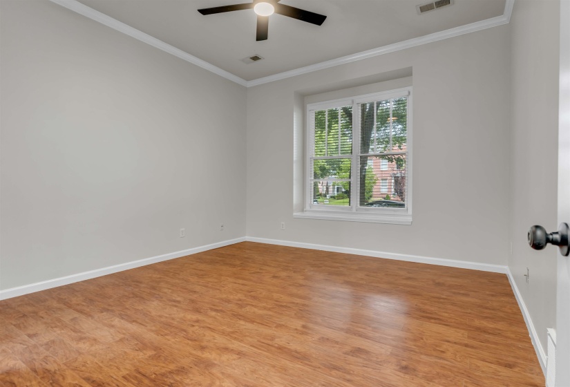Room featuring wood-finish flooring, light grey painted walls, white crown molding, and a ceiling fan with integrated lighting