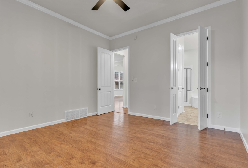 Spacious room featuring wood-finish flooring, white baseboards, and crown molding
