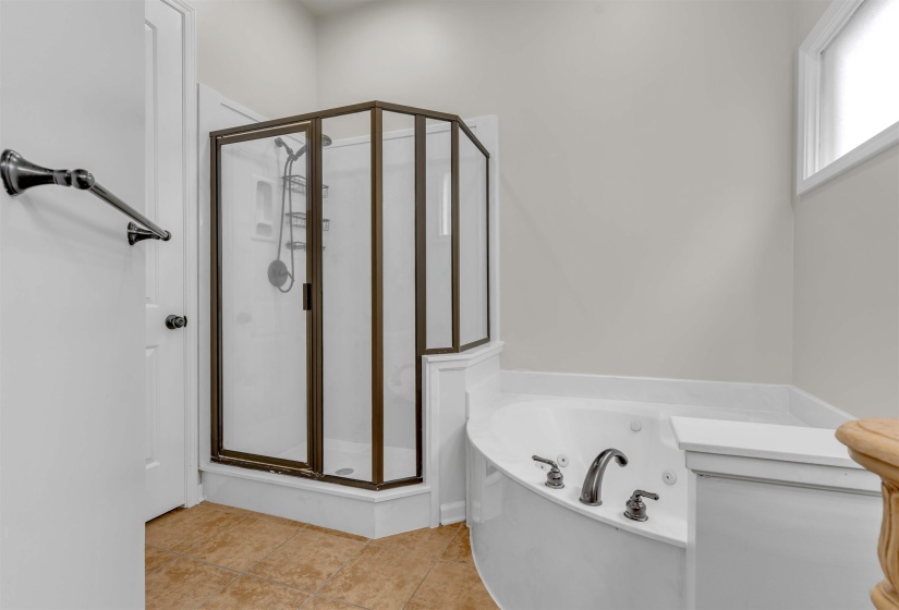 Corner shower enclosure with dark bronze framing, an adjacent built-in soaking tub with a curved front, and coordinating dark bronze fixtures