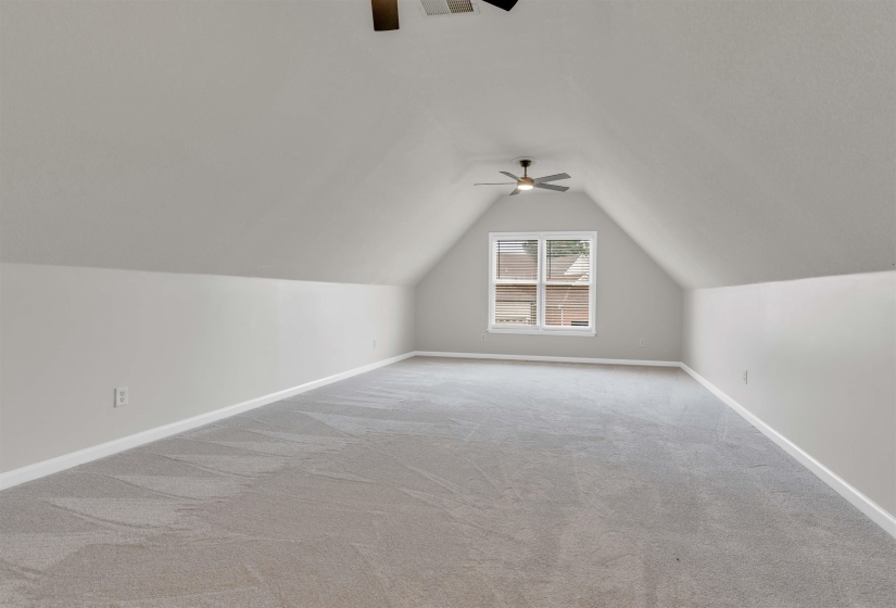 Spacious bonus room featuring sloped ceilings, light gray carpeting, and a window providing natural illumination