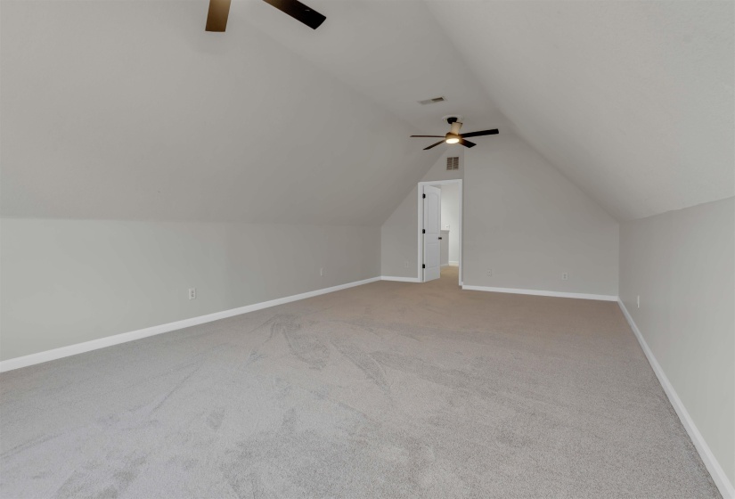 Spacious loft area featuring sloped ceilings, two ceiling fans with integrated lighting, neutral wall tones, and plush carpeting