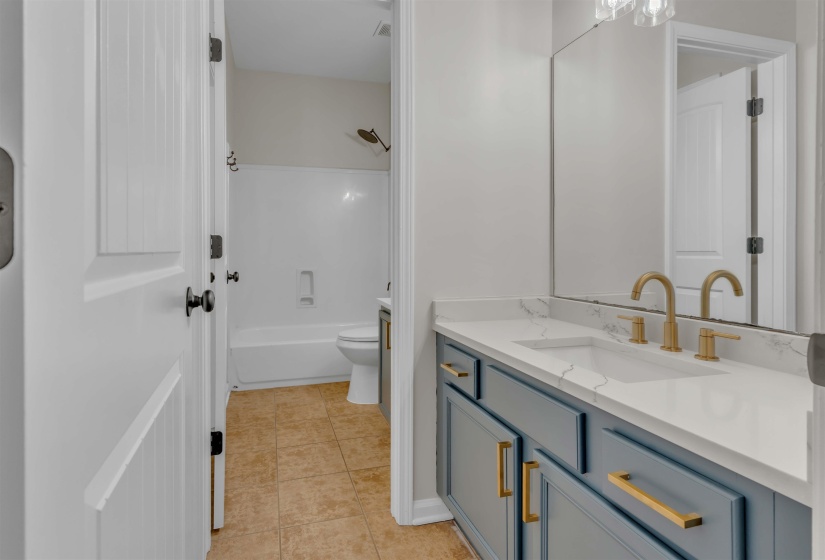 Bathroom vanity featuring a light blue cabinet with gold hardware, a white countertop with an integrated sink, and a gold-finish faucet
