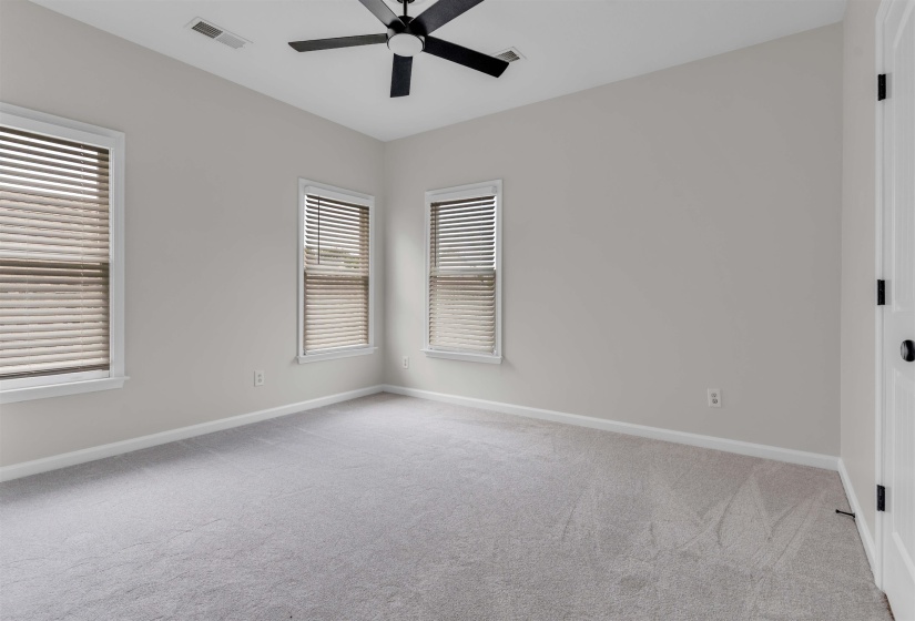 Neutral-toned room featuring a light gray carpet, multiple windows with blinds, a black ceiling fan, and white trim