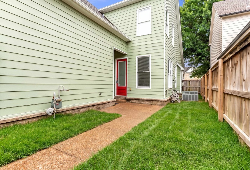 Side yard featuring a concrete path, green lawn, wood privacy fence, and light green siding