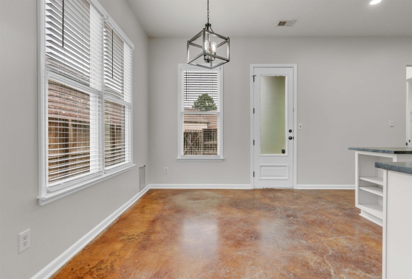 Spacious interior with acid-stained concrete flooring, multiple windows with blinds, a full-lite door, and a geometric pendant light fixture