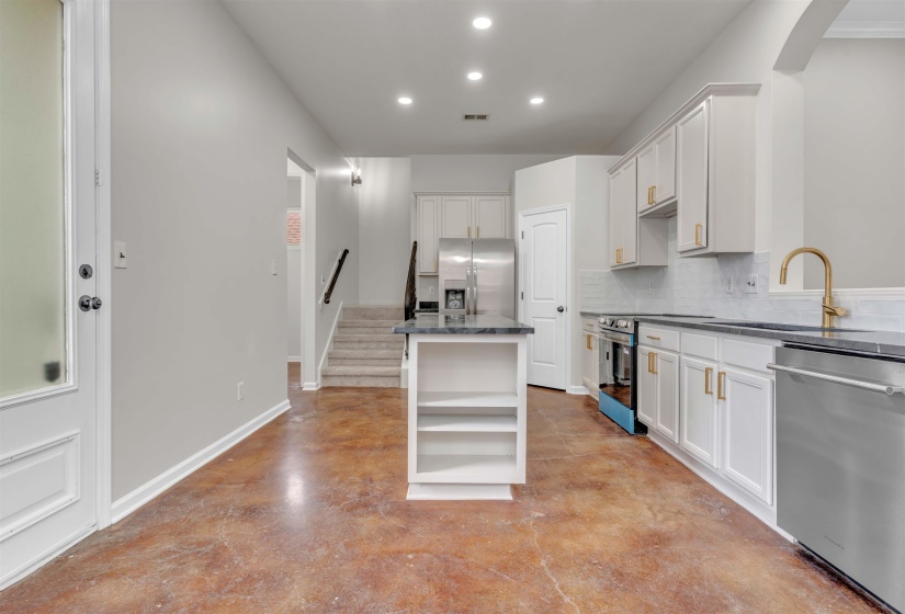 Kitchen featuring white cabinetry, dark countertops, a gold-tone faucet, stainless steel appliances, and a central island with open shelving