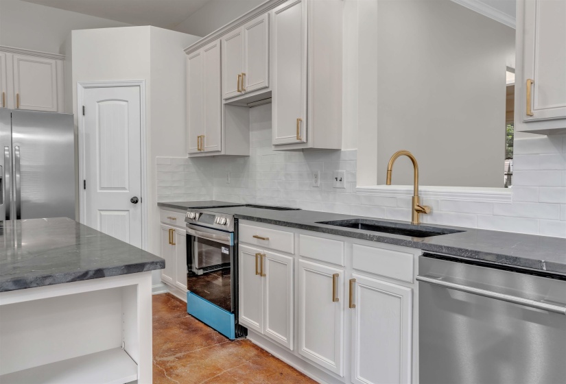 Modern kitchen featuring white cabinetry with gold-tone hardware, dark countertops, and a white subway tile backsplash