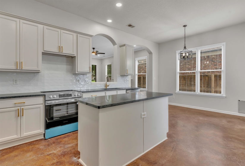 Kitchen featuring light-toned cabinetry, a subway tile backsplash, dark countertops, and a central island
