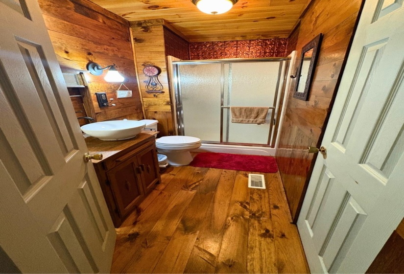 Bathroom featuring wood-finish wall and ceiling panels, a shower enclosure with sliding glass doors, a vanity with a vessel sink, and wide plank wood-finish flooring