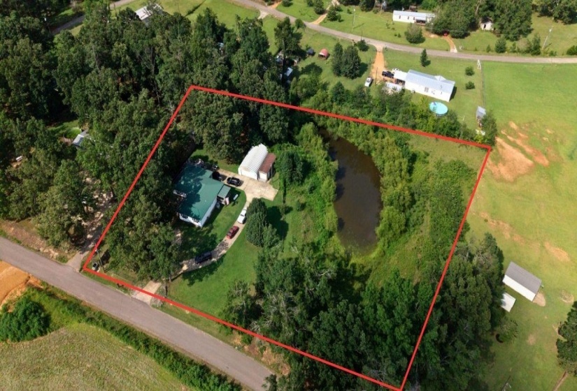 Aerial property view featuring a main residence, an accessory building, a private pond, mature trees, and an expansive grassy area