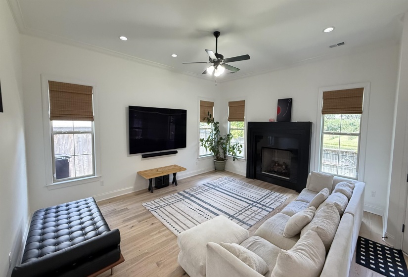 Living area featuring plenty of natural light, light wood-style floors, ceiling fan, a fireplace, and ornamental molding