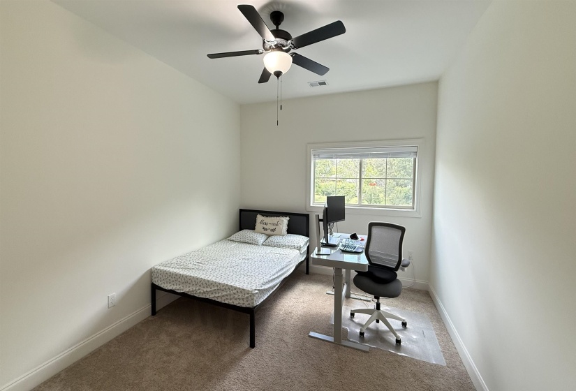 Carpeted bedroom featuring an office area and a ceiling fan