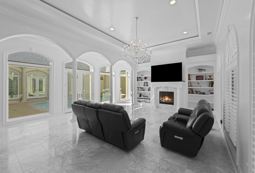 Living room with a raised ceiling, ornamental molding, a high end fireplace, marble tiled floors, and a chandelier