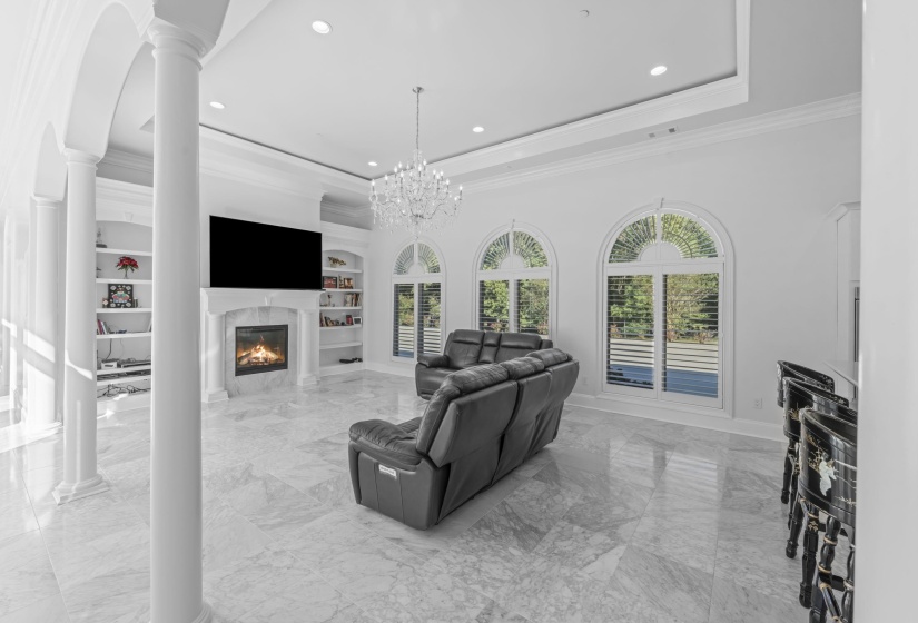 Living room featuring light marble finish floors, crown molding, a raised ceiling, a high end fireplace, and built in shelves