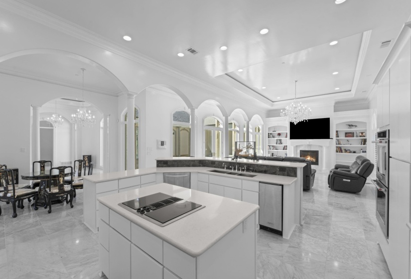 Kitchen with a chandelier, a tray ceiling, open floor plan, a glass covered fireplace, and crown molding