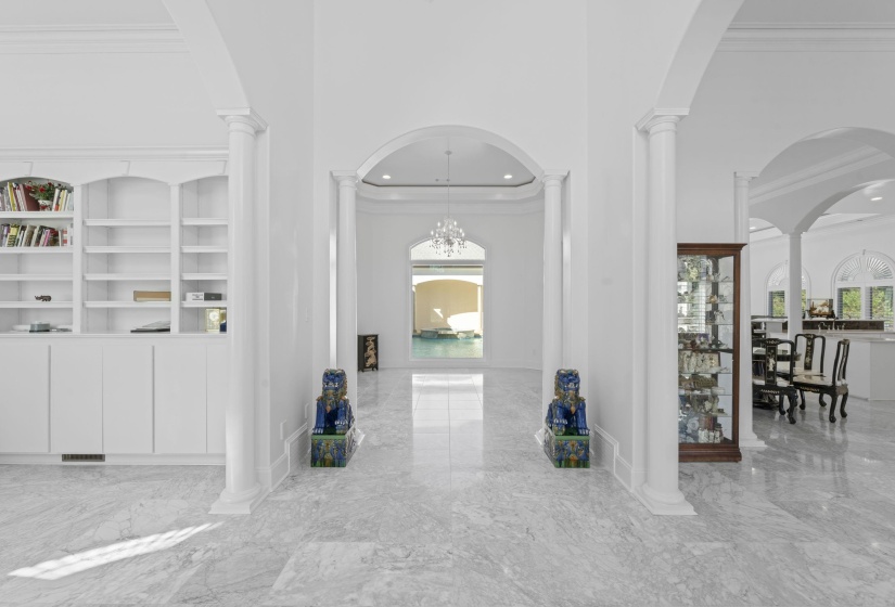 Hallway with a towering ceiling, light marble finish flooring, crown molding, arched walkways, and decorative columns