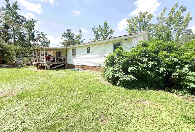Spacious grassy yard with mature trees and a covered rear deck featuring wooden railings and support posts